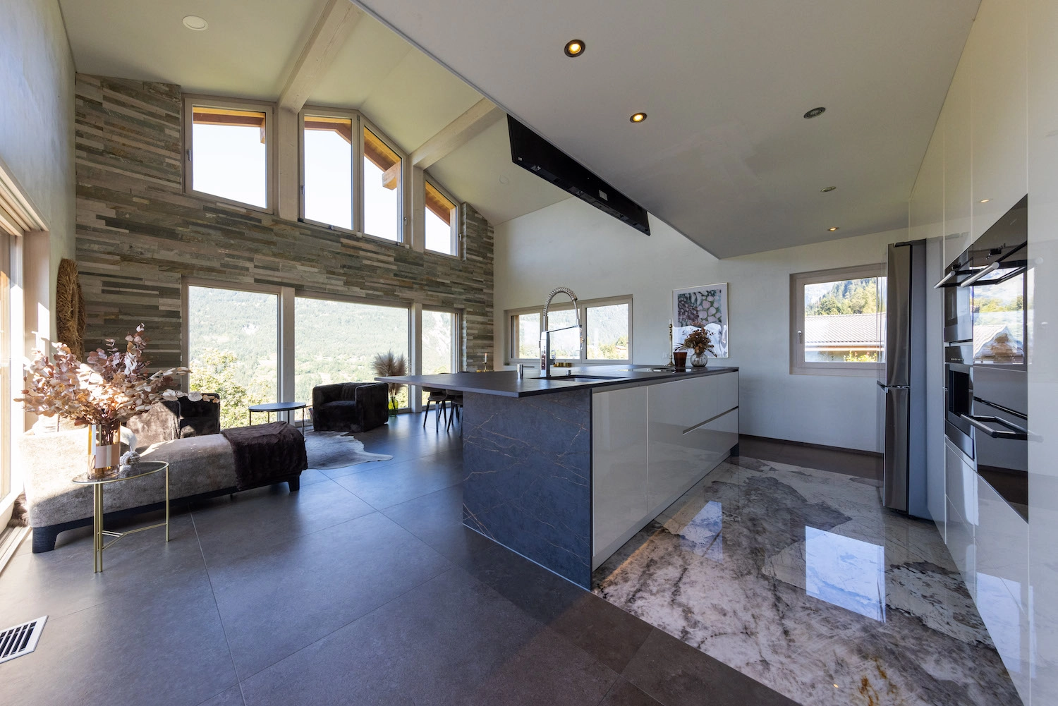 Pose de carrelage intérieur moderne grand format dans un salon ouvert sur la cuisine par Millius Groupe en Valais
